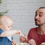 Baby sitzt im Hochstuhl und probiert erste feste Nahrung